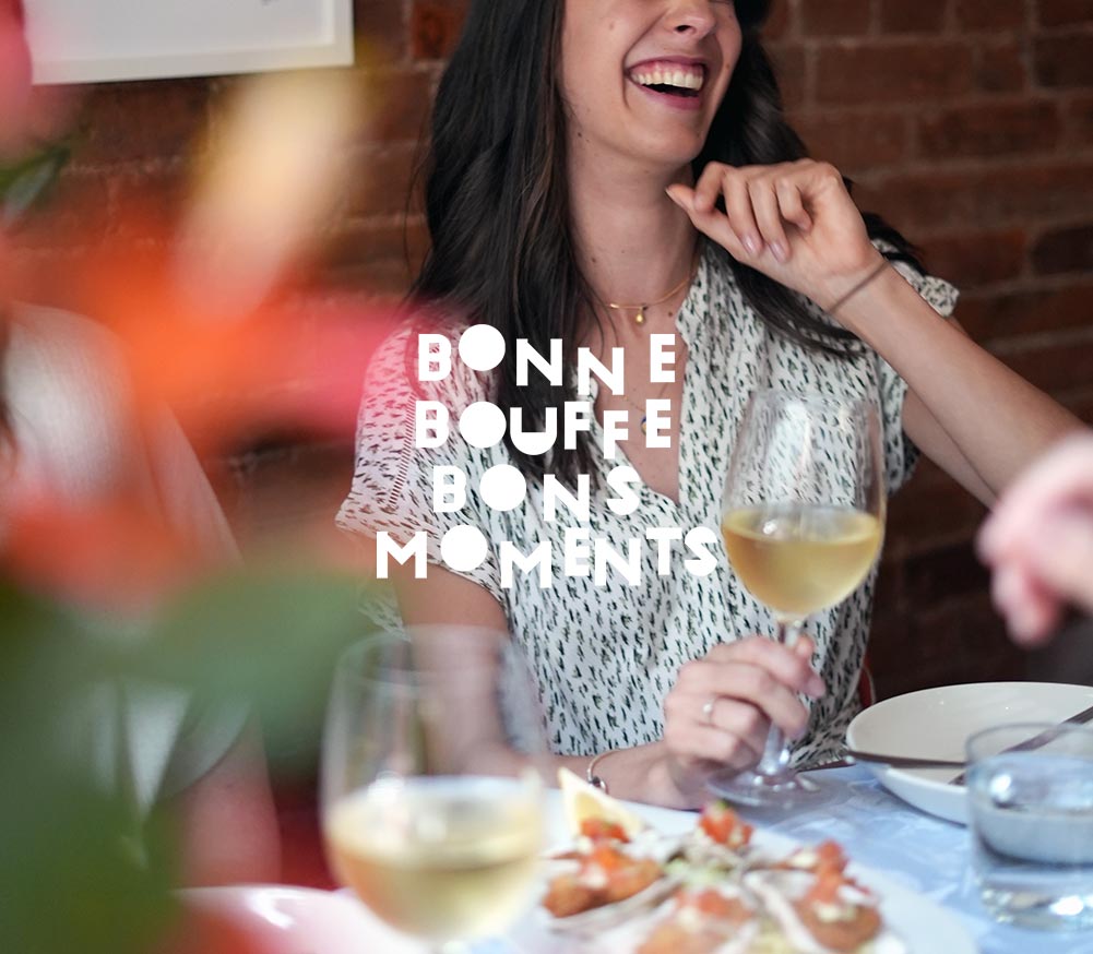 Jeune femme riant avec verre de vin blanc et table avec huîtres dans le Vieux Montréal avec le titre BONNE BOUFFE BONS MOMENTS